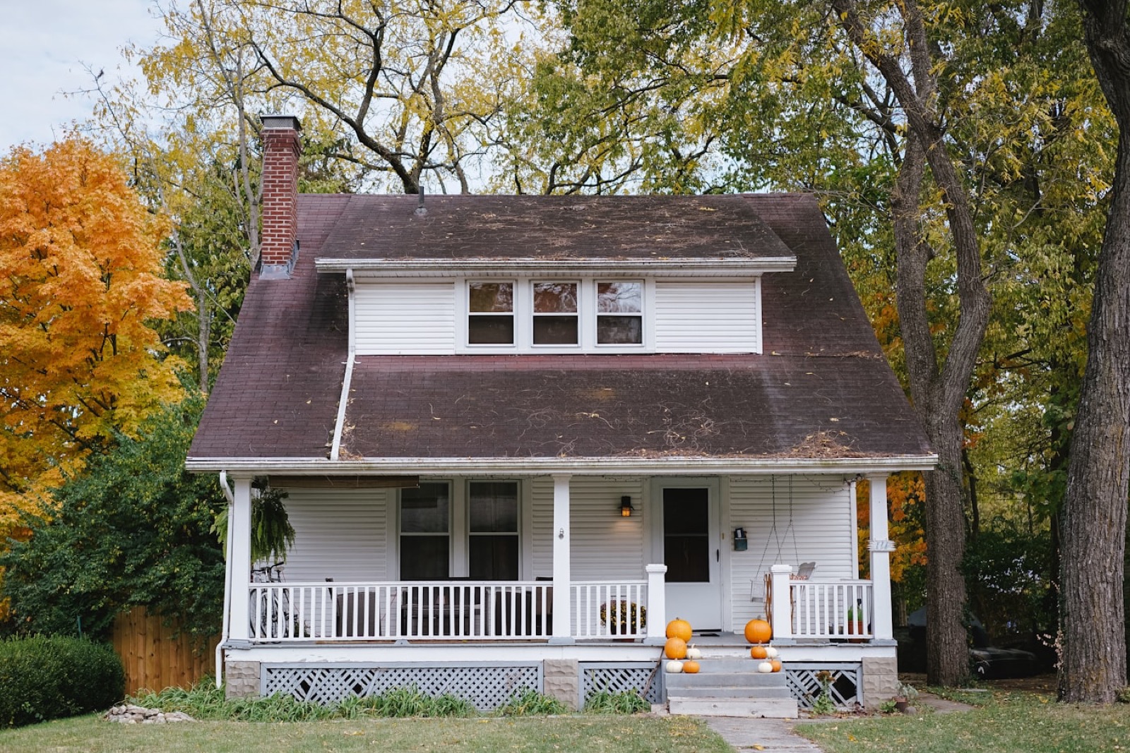 An older bungalow with a plain lawn and bare foundation